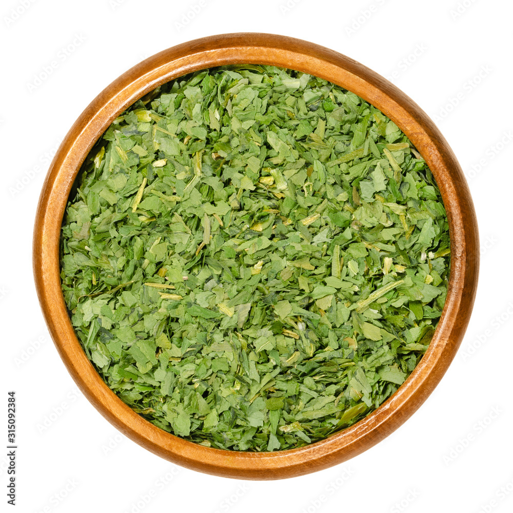 Dried ramsons in wooden bowl. Shredded leaves of Allium ursinum, also called buckrams, wild garlic or bear leek. Wild relative of chives native to Europe and Asia. Macro food photo closeup over white.