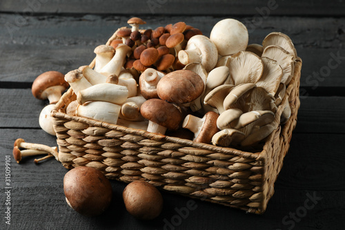 Different mushrooms in basket on wooden background, close up