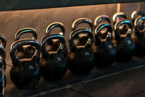 For you to choose. Stylish kettlebells weights made of black leather and iron lying in a row on the shelf in workout gym. Sport, lifting, healthy lifestyle concept. Horizontal shot.