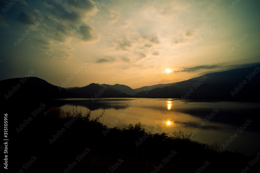Mountain, sky and river in a quiet and cool atmosphere. Similar color scheme .View of blue mountains with reflection in lake . Landscape with blue mountains near lake in Sukhothai Thailand Mountain, sky and river in a quiet and cool atmosphere. Similar color scheme .View of blue mountains with reflection in lake . Landscape with blue mountains near lake in Sukhothai Thailand
