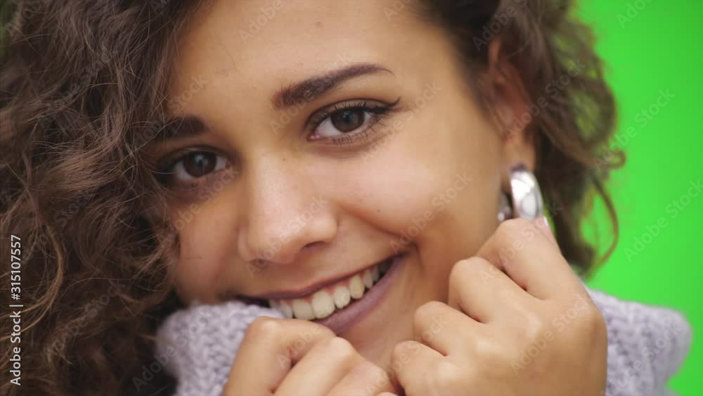Shy afro-american girl is smiling widely. She is warming up lower part of face, wearing white sweater. Close up. Copy space. Shy afro-american girl is smiling widely. She is warming up lower part of face, wearing white sweater. Close up. Copy space.