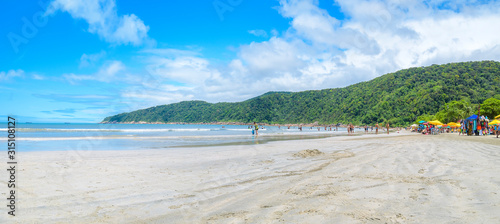 Fototapeta Naklejka Na Ścianę i Meble -  People at a Brazilian beach on a sunny day. Panoramic view. Beach with a calm sea and few waves at Praia do Guaiuba beach - Guaruja SP Brazil.