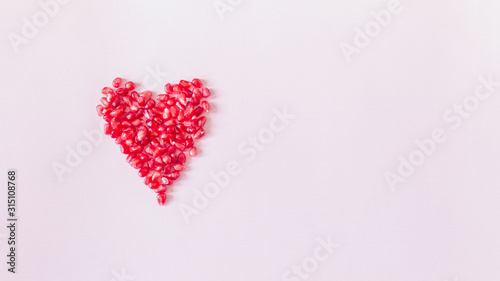 abstract delicate pink background with a heart lined with pomegranate seeds top view. pomegranate seeds lay flat. copy space.