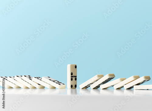 Dominos falling around standing domino against blue background