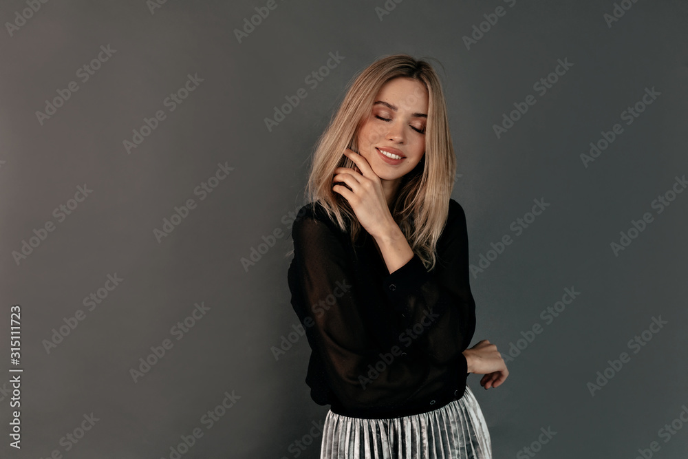 Satisfied lovely woman with blond hair wearing black shirt posing with closed eyes and smile over isolated grey background Satisfied lovely woman with blond hair wearing black shirt posing with closed eyes and smile over isolated grey background