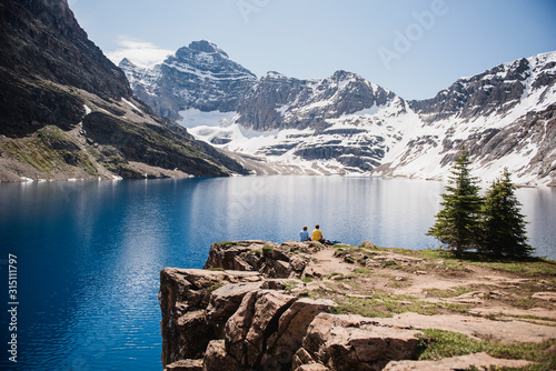 Couple sitting on cliff overlooking tranquil, sunny mountains lake, Yoho Park, British Columbia, Canada