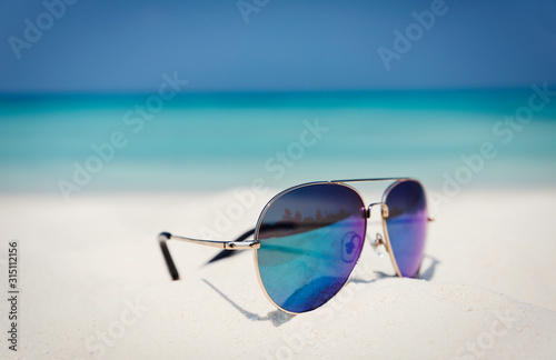Close up aviator sunglasses in sand on sunny tropical ocean beach