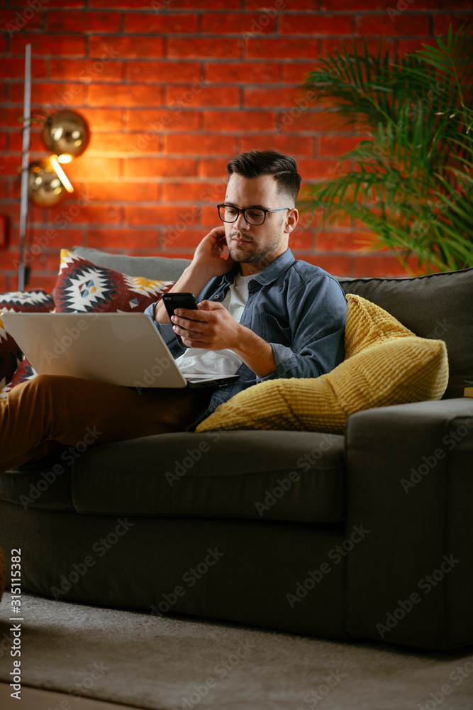 Young man working from home. Businessman at home on sofa with laptop and phone. Young man working from home. Businessman at home on sofa with laptop and phone.