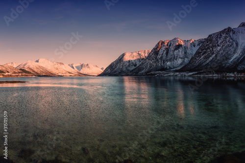 Amazing winter landscape with rocky snowy mountains in sunset light, blue sky and reflection in water, Lofoten Islands, Norway. Outdoor travel background