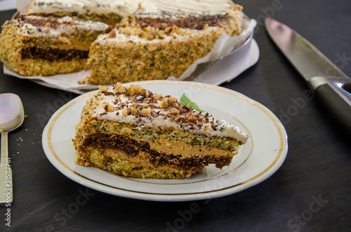 Tasty piece of cake with condensed milk and poppy seeds on a plate on a black table. Knife and spoon on the table. Close-up.