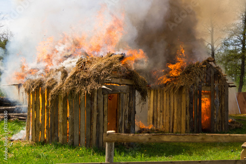 Two wooden buildings with thatched roofs burn in flames