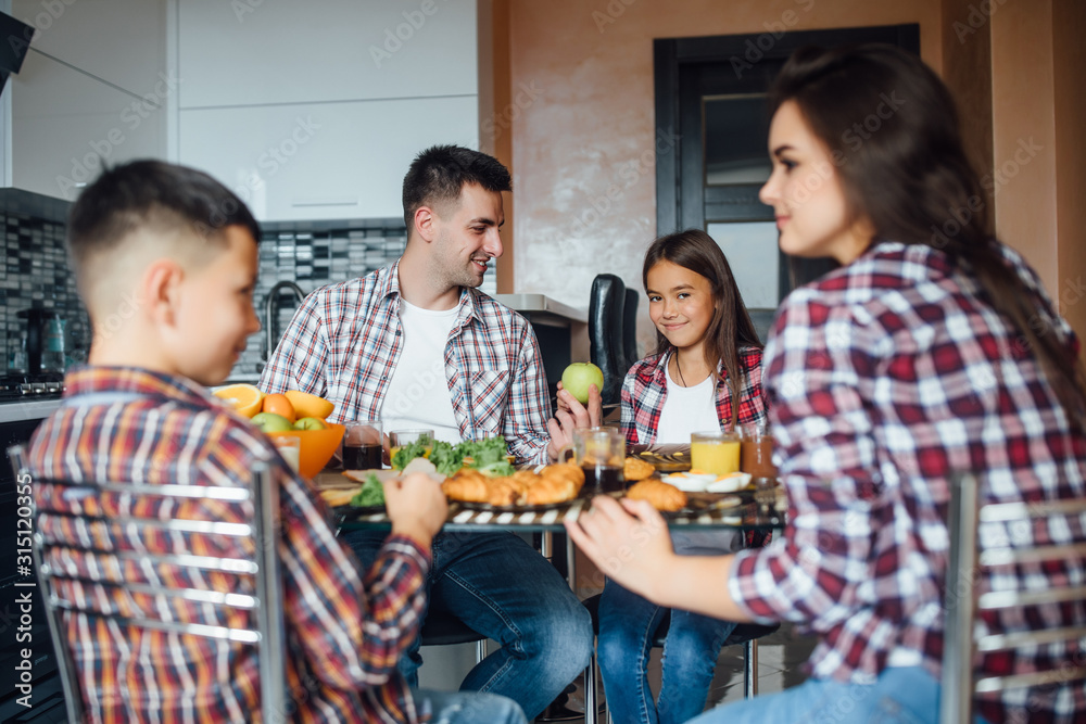 Obraz premium Cheerful man and woman eating food with children during breakfast at home. Family concept.