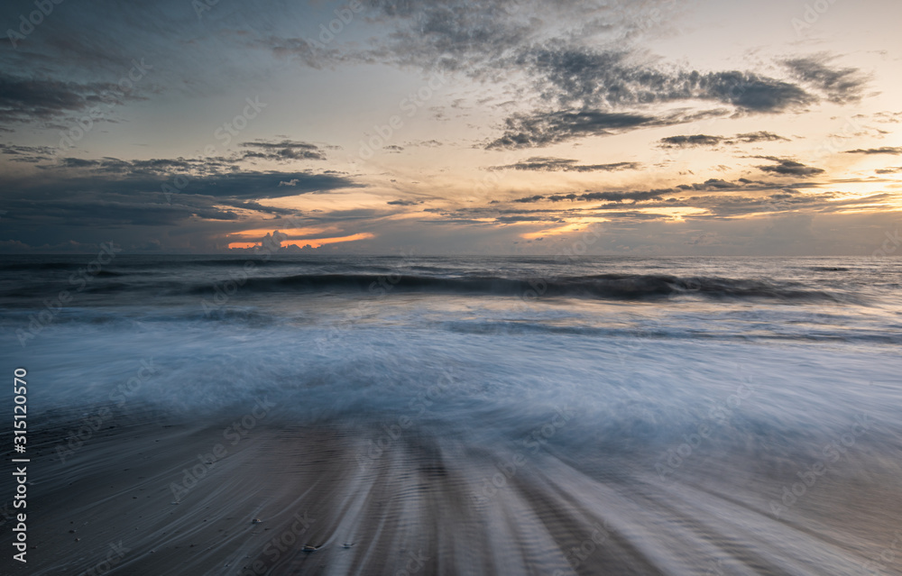 Fototapeta premium Seawaves splashing on the coast during a dramatic sunset