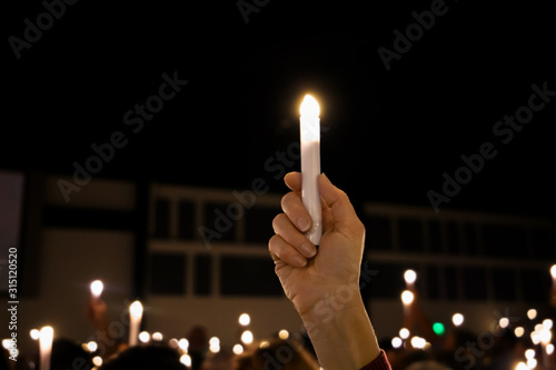 One single hand arm holding up a LED candle amongst a crowd of lights at a candlight service vigil