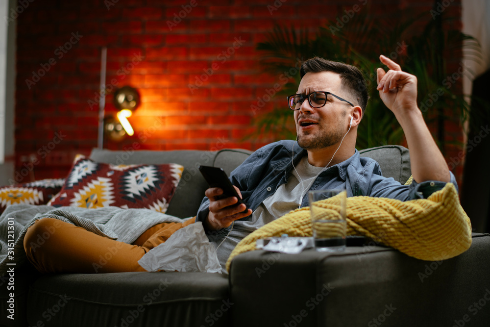 Fototapeta premium Young man listening music. Attractive man sitting on sofa and listening music in living room.