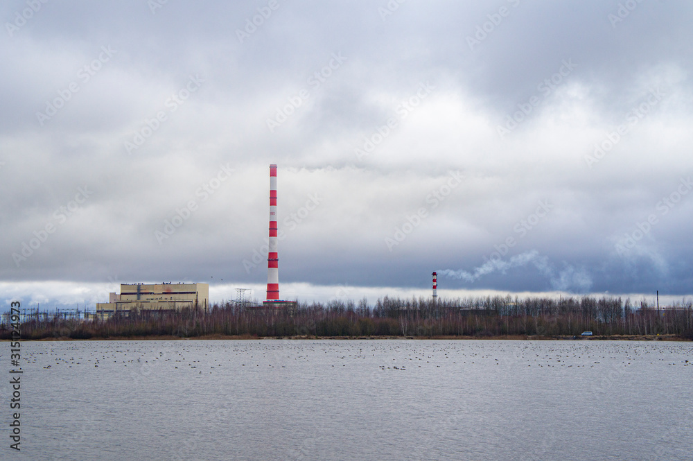 Red-white factory chimney near a winter lake.