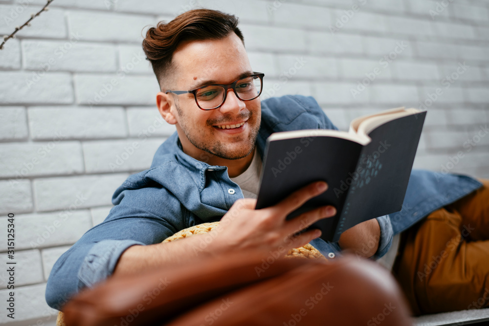 Young man reading book. Handsome student preparing exam on a floor of the living room. Young man reading book. Handsome student preparing exam on a floor of the living room.