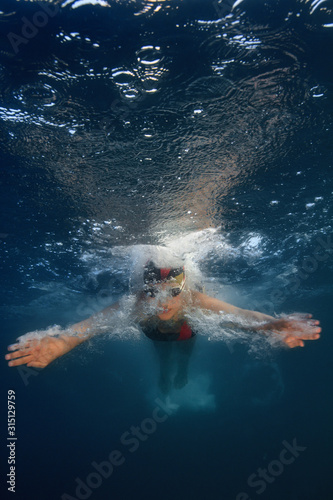 Professional swimmer moving fast in ocean water deep blue color on background, underwater shot