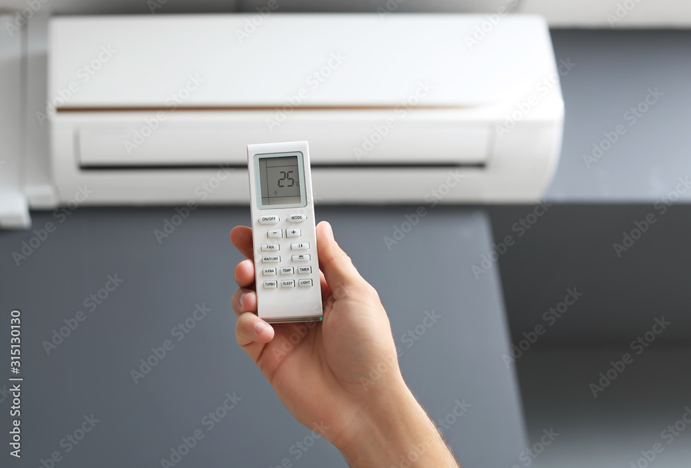 Young man switching on air conditioner at home