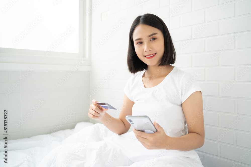 Pay shopping online by credit card,Young Asian woman use internet smartphone and card messaging text credit number and smiling while lay on bed in bedroom at home,lifestyle Social networks. Pay shopping online by credit card,Young Asian woman use internet smartphone and card messaging text credit number and smiling while lay on bed in bedroom at home,lifestyle Social networks.