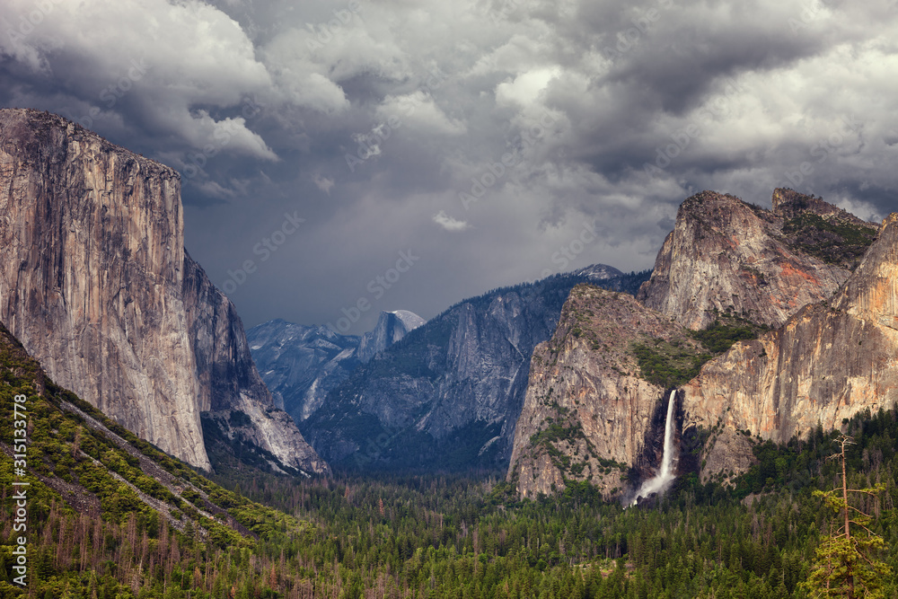 Classic view of scenic Yosemite Valley with famous El Capitan and Half Dome rock climbing summits and Bridal Vei waterfall, with a storm in the background, Yosemite National Park, California