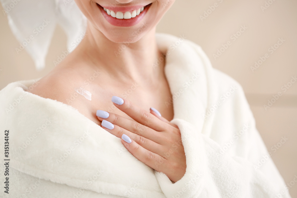 Beautiful young woman applying cream on her shoulder in bathroom, closeup