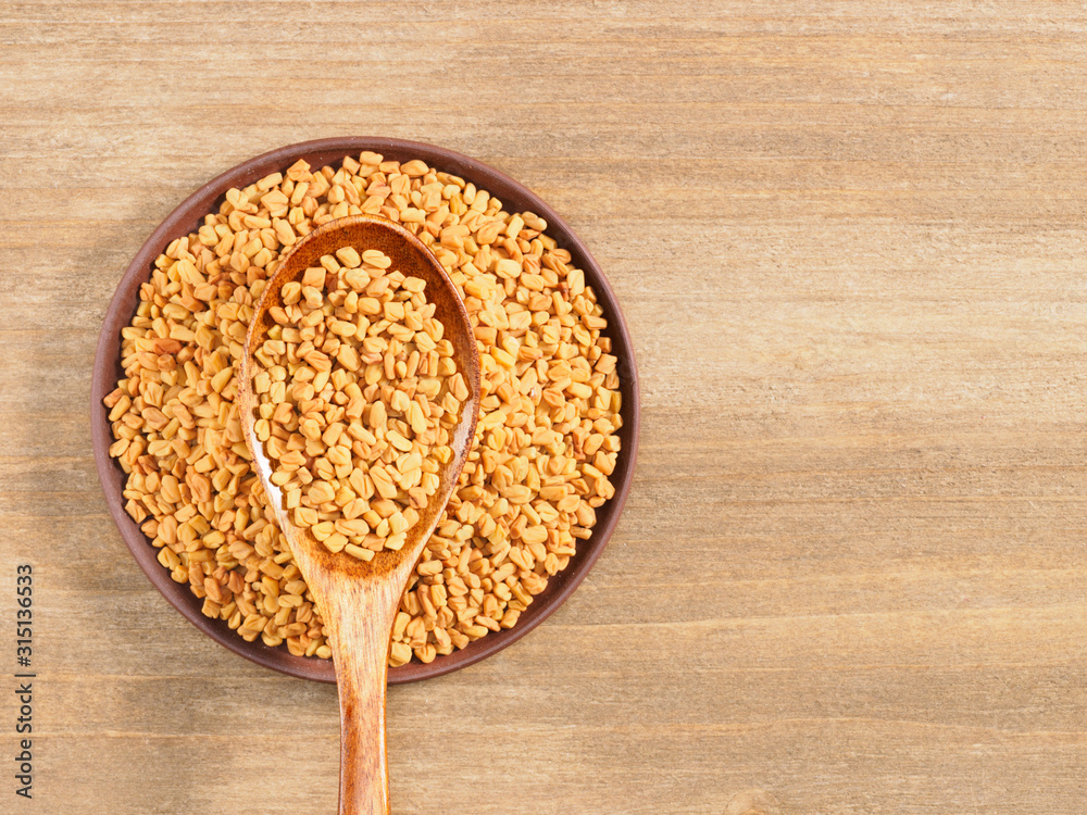 Fenugreek in clay plate and spoon on a brown wooden background. Indian cuisine, ayurveda, naturopathy, modern apothecary concept Fenugreek in clay plate and spoon on a brown wooden background. Indian cuisine, ayurveda, naturopathy, modern apothecary concept