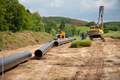 Unplugged gas pipeline in the coutryside diagonally from the left diagonally by photo with gas laying machines in the background