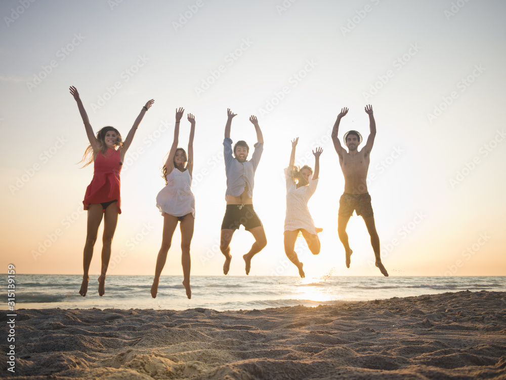 Five friends jumping on the beach at sunset on summer