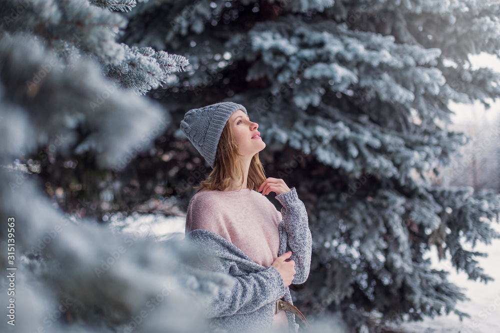 winter mood. A woman in  winter funny hat looks up. Walk December January February. Snowy tree spruce branches park walk. Beautiful girl in pink sweater. Place for text banner. dreams magic fairy tale