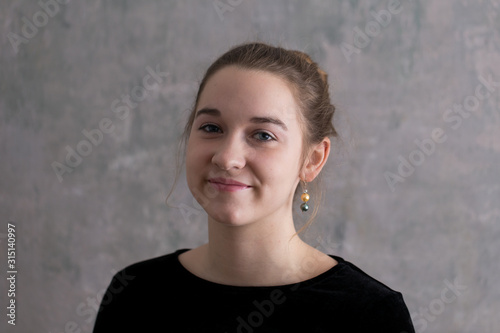 Closeup portrait of pretty smiling young woman with dirty blond hair up in a bun wearing a black dress and pearl pendant earrings