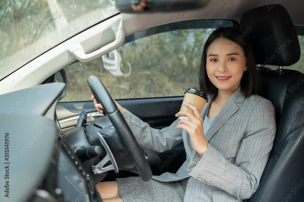 Asian female driver smiling and drinking coffee in the car, Beautiful girl  holding an eco paper coffee cup,looking to camera while driving her car, happy life transport in city