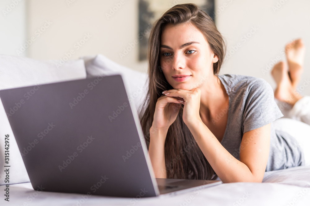 Smiling young woman laying on couch and using laptop Smiling young woman laying on couch and using laptop