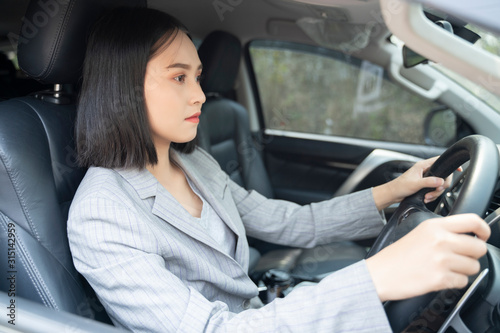 Safety driving concept, Smiling happy young Chinese Thai Asian businesswoman driving a car in town, Confident and beautiful girl. Rear view woman in business suit wear looking over her shoulder