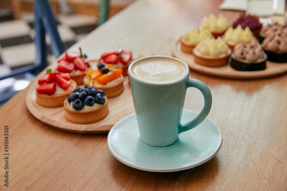 a white cup with a coffee is on a saucer, next to a plate are cupcakes with berries a white cup with a coffee is on a saucer, next to a plate are cupcakes with berries