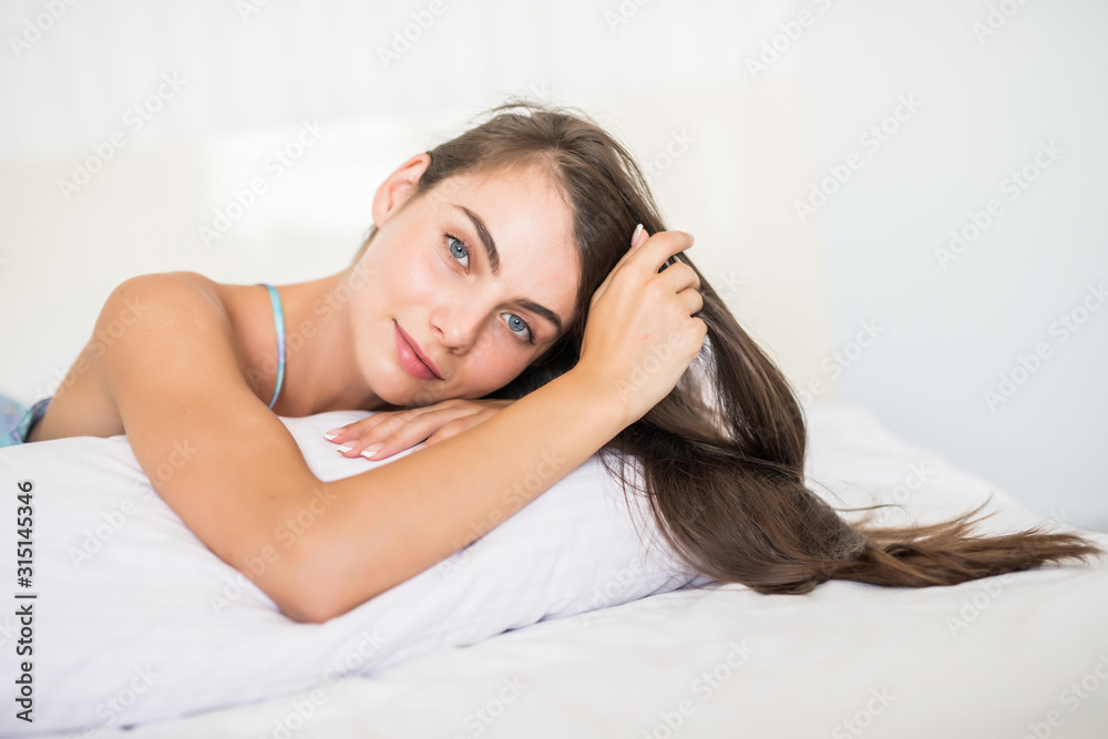 Smiling casual brunette woman lying in her bed in bright bedroom Smiling casual brunette woman lying in her bed in bright bedroom