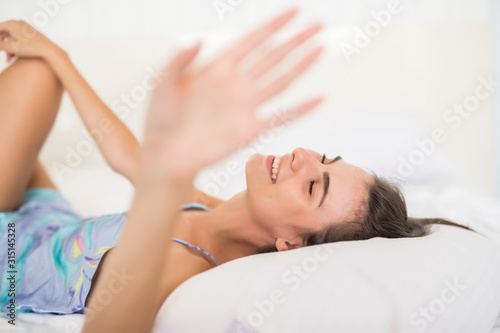 Young pretty woman lying in underwear in white bed and cover camera with hands