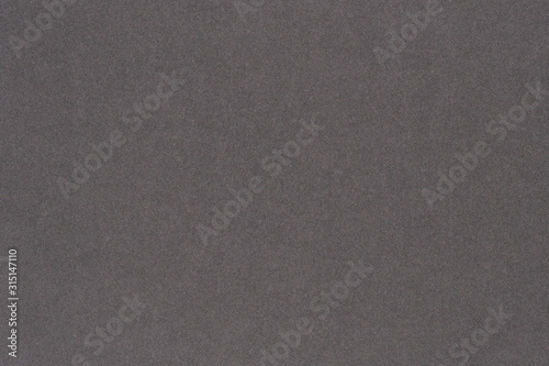 Gray colored paper. Texture of surface, fibers and irregularities are visible. View from above. Dark background or wallpaper