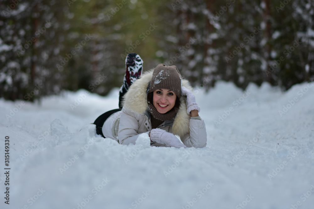 Fototapeta premium Beautiful girl in the winter frosty forest lies in the snow