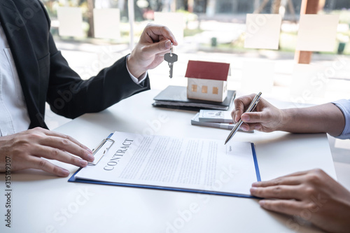 Real estate agent are presenting home loan and giving house, keys to customer after signing contract to buy house with approved property application form