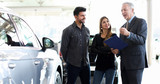 Car dealer exaplining a car's features to a couple by reading a document