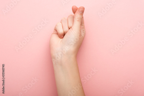 cropped view of woman showing heart gesture on pink background