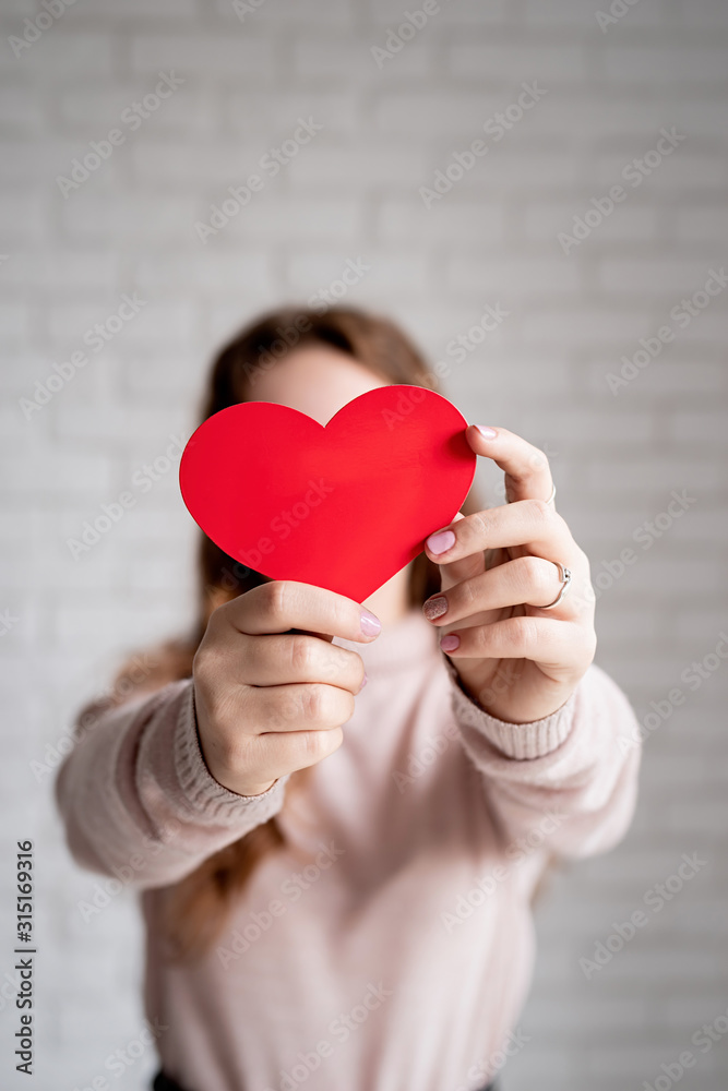 young woman holding a red heart shape in front of her face young woman holding a red heart shape in front of her face