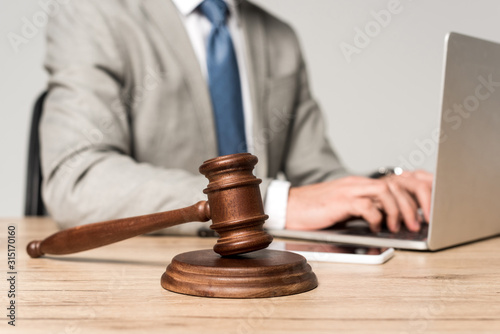 selective focus of gavel near lawyer working at laptop isolated on grey