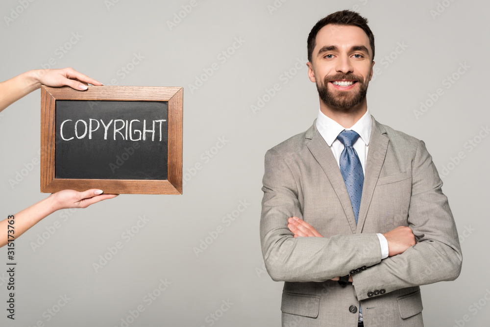 partial view of woman holding chalkboard with copyright inscription near businessman smiling at camera isolated on grey partial view of woman holding chalkboard with copyright inscription near businessman smiling at camera isolated on grey