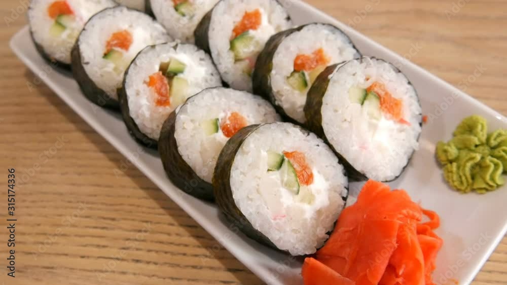 Large sushi rolls in nori with salmon, crab sticks, cucumbers, philadelphia cheese. Nearby is green wasabi and red ginger. Japanese food Large sushi rolls in nori with salmon, crab sticks, cucumbers, philadelphia cheese. Nearby is green wasabi and red ginger. Japanese food