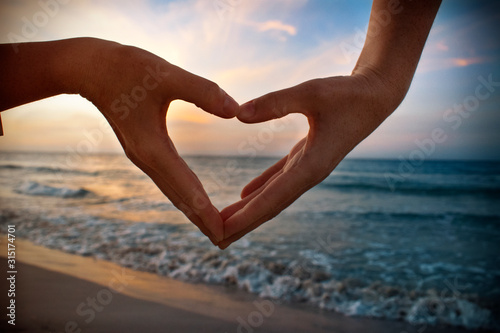 Photography heart in hands on beach at sunset