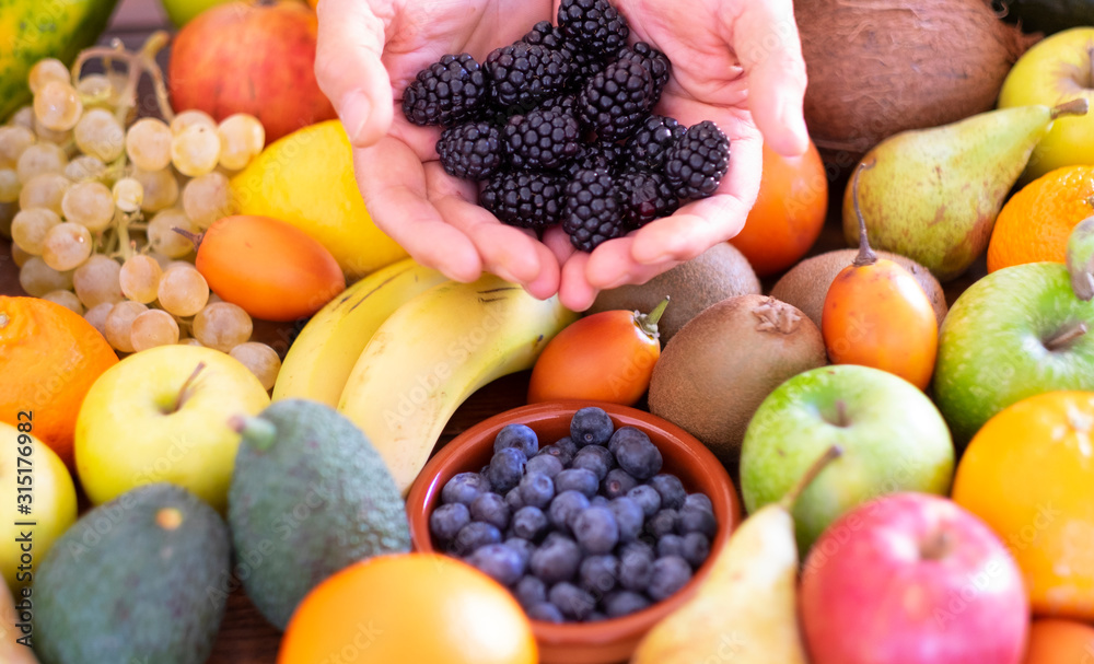 A Caucasian person holds a group of fresh blackberries in his hands. Background with an assortment of healthy freshly picked fresh fruit. Vegan or vegetarian choice. A Caucasian person holds a group of fresh blackberries in his hands. Background with an assortment of healthy freshly picked fresh fruit. Vegan or vegetarian choice.