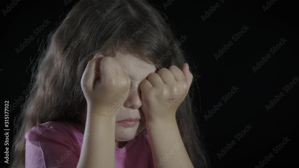 Wipe away the tears. A little girl cries and rubs her eyes on a black background. Wipe away the tears. A little girl cries and rubs her eyes on a black background.
