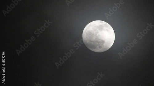 Full moon on dark cloudy night. Clouds passing by the moon, real time shot.